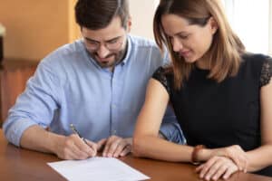 Pleasant young woman watching smiling husband signing contract